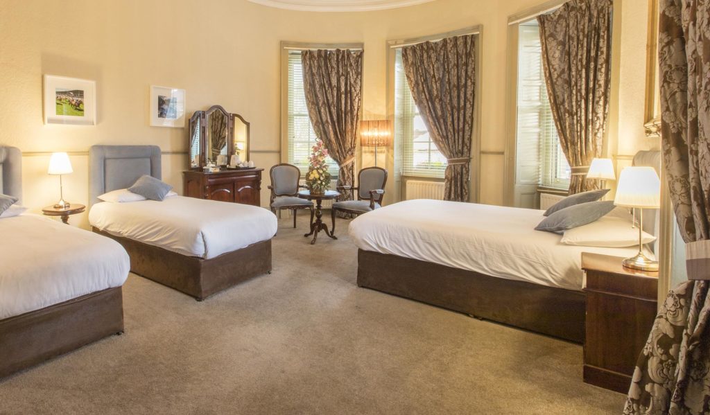 Spacious triple room with three single beds, tall bay windows and a seating area at the Silken Rooms in Kildare town